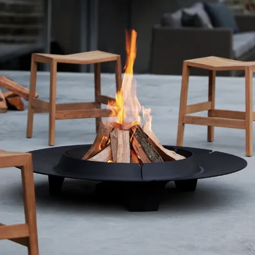 Round black cast iron fire pit on a patio surrounded by low teak stools