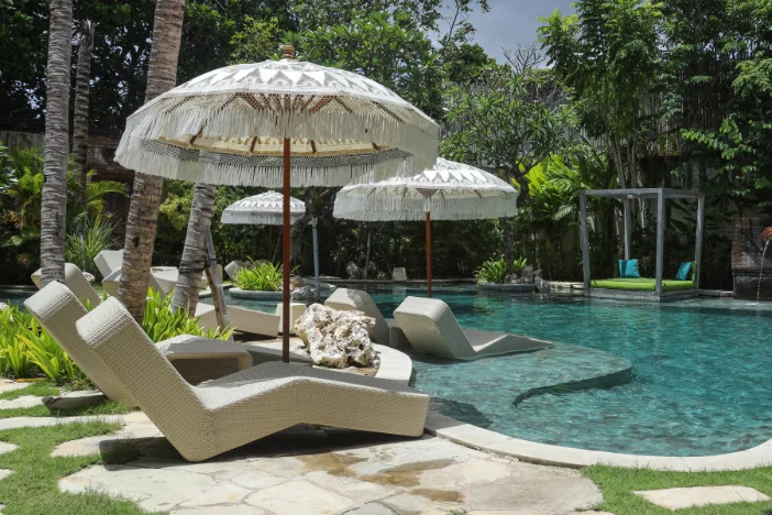 Angular minimalist modern sun loungers with coordinating white fringe patio umbrellas around a tiled pool