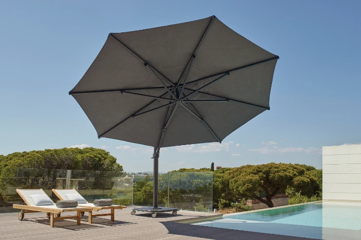 Large dark grey cantilever patio umbrella with coordinating round canopy next to two sunloungers and a pool