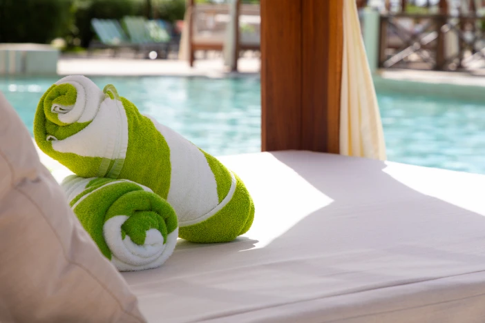Carefully rolled plush lime green and white beach towels sitting on a poolside cabana bed