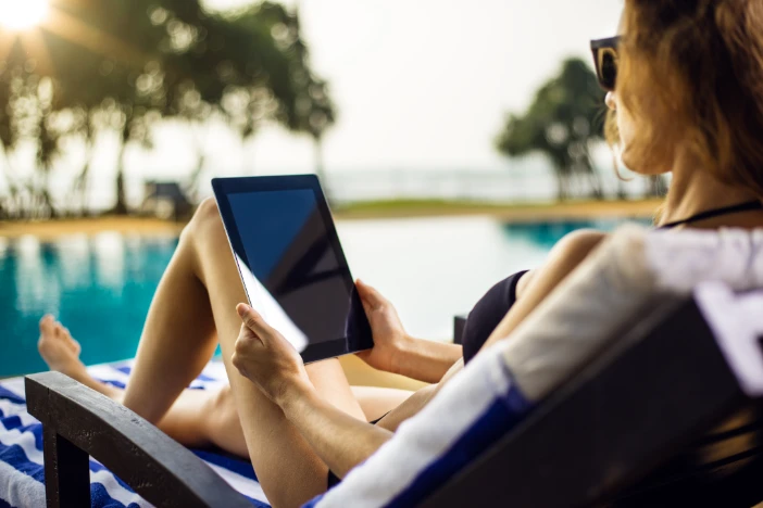Woman sitting on sunlounger next to a pool using a computer tablet