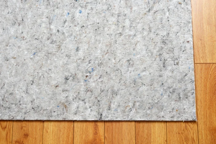 Grey flecked felt rug pad on a honey-colored hardwood floor