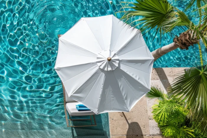 Outdoor umbrella with white canopy next to a swimming pool and palm trees