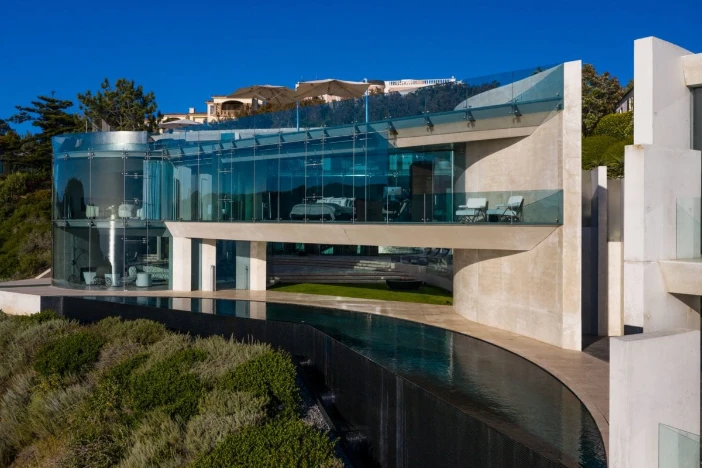 Side view of ultra modern multi-level mansion with floor-to-ceiling glass and white concrete walls with an infinity pool