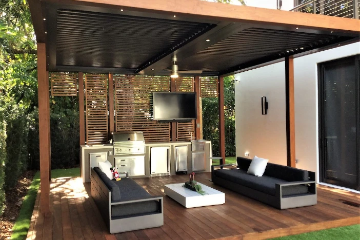 Standalone modern wooden pergola with facing sofas, stainless steel grill, TV, recessed lights and a ceiling fan