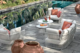 Contemporary curved outdoor lounge set with metal rod bodies and white and salmon cushions around two round accent tables