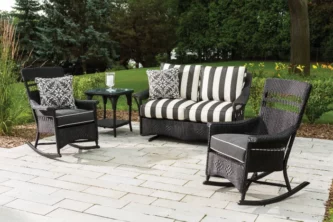 Black all-weather wicker rocking chairs and loveseat with striped upholstery and coordinating accent pillows on a backyard patio