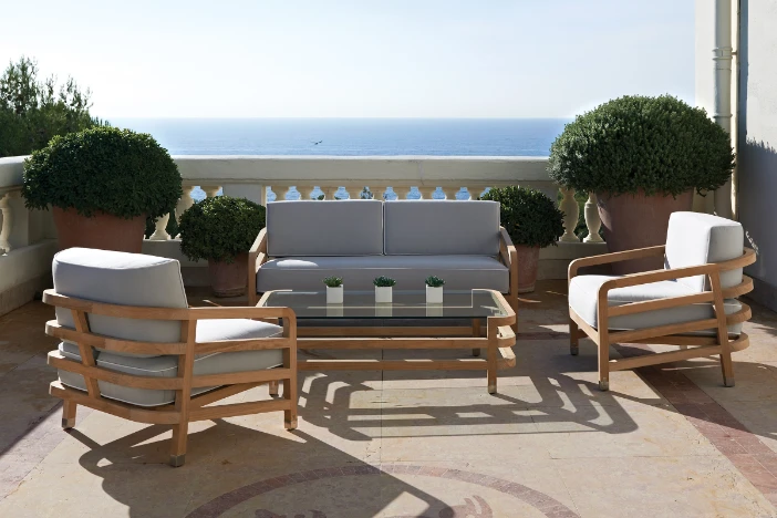 Modern outdoor lounge chairs and loveseat with open wood frame and plush light grey upholstery with matching coffee table on a seaside veranda