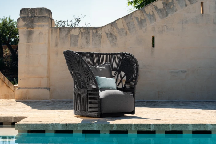 Dark brown woven outdoor lounge chair with wide flaring wraparound backrest sitting poolside