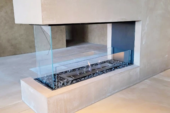 End of a concrete wall with peninsula style bio-ethanol burning fireplace insert with grey decorative media surrounding the burner