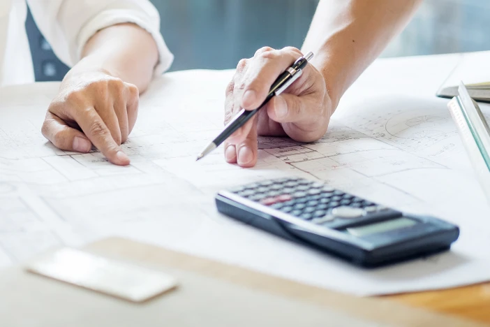 Close-up of man and woman reviewing a floor plan on a table with a calculator and pen