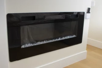 Wide black frames electric fireplace insert with clear decorative glass media on white wall