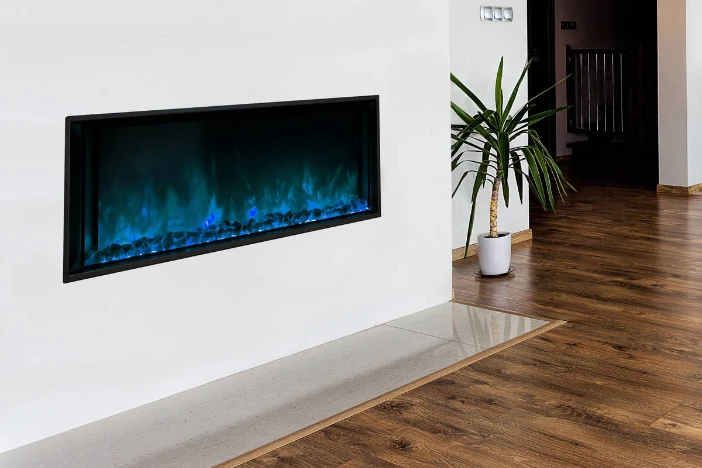 Modern electric fireplace insert with blue flame on white wall in in room with hardwood floors