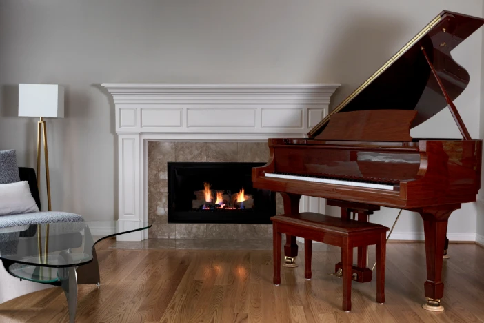 Gas fireplace insert with marble framing and white mantle in room with hardwood floors and baby grand piano