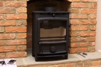 Black iron fireplace inset being installed in red brick wall with tools and a mobile phone sitting on the hearth