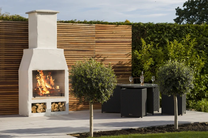 Traditional outdoor wood-burning fireplace made of white concrete against a wood slat wall near a dining set