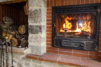 Iron wood-burning fireplace insert set in brick wall near firewood and fire tools