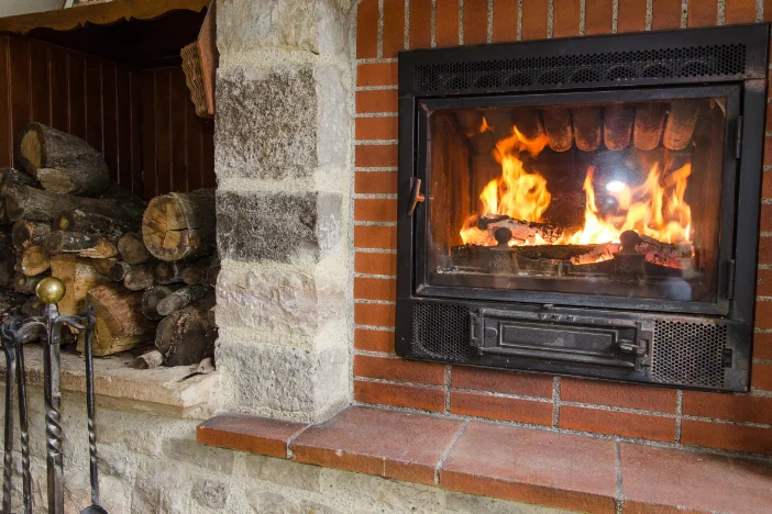 Iron wood-burning fireplace insert set in brick wall near firewood and fire tools