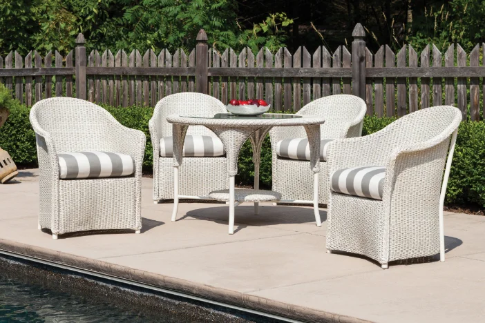 Four white resin wicker armchairs around a matching round table near a pool