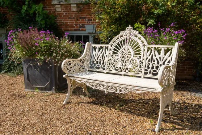 Ornate white-painted wrought iron bench on rust gravel in an English garden