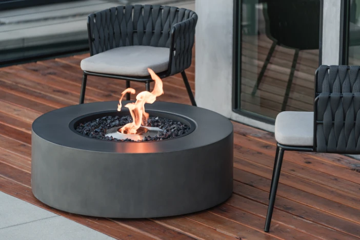 Round concrete composite fire table with flame on a hardwood deck near patio lounge chairs