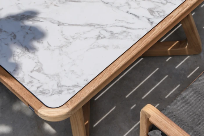 Close-up of wood-framed patio dining table with white marbled high-pressure laminate top.