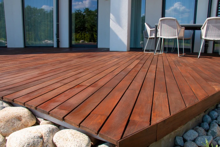 Reddish brown ipe hardwood deck surrounded by stones with white all-weather wicker chairs