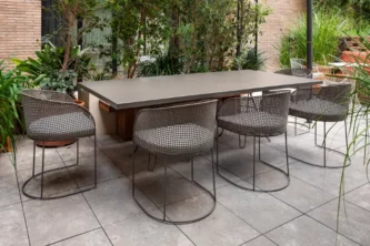 Wireframe outdoor dining chairs with perforated metal bodies alongside a rectangular table on a patio