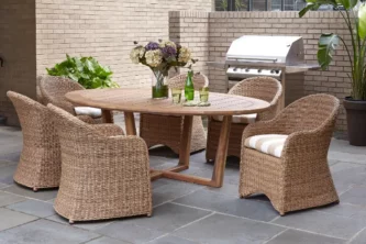 Natural looking all-weather wicker dining chairs around a wooden table near a barbecue on a patio