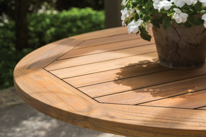 Round teak patio table with slats and a flower pot in the center