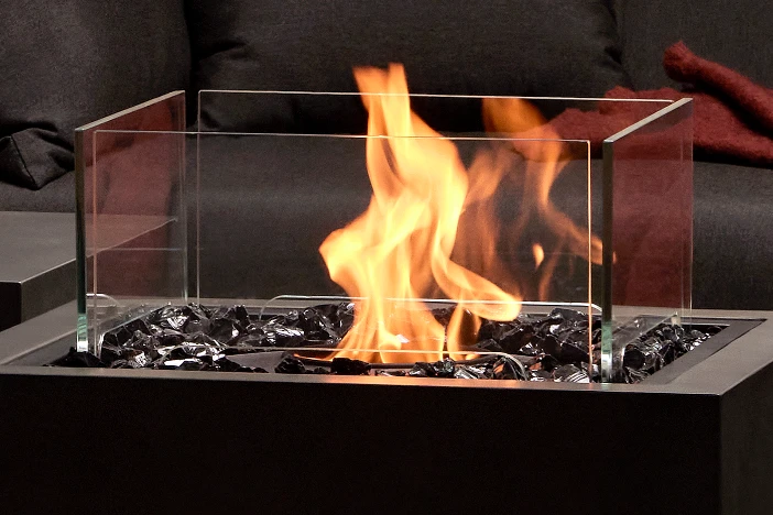 Clear glass rectangular wind screen protecting a flame on a dark fire pit table