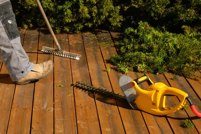 Person sweeping a hardwood deck with a yellow trimmer and pruned branches nearby