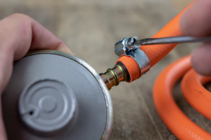 Person using a small screwdriver to adjust the connection between an orange hose and a propane tank regulator