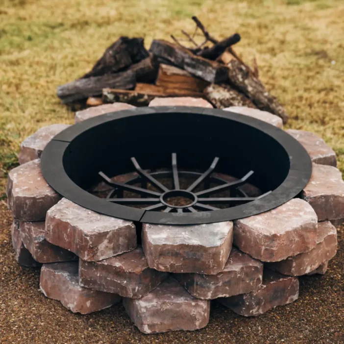 Black metal grate set in round stacked stone fire pit near firewood