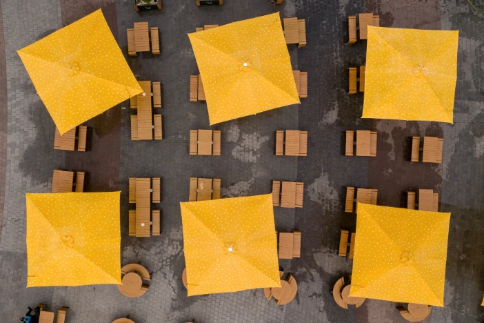 Overhead view of six outdoor umbrellas with square yellow canopies shading sets of tables and chairs