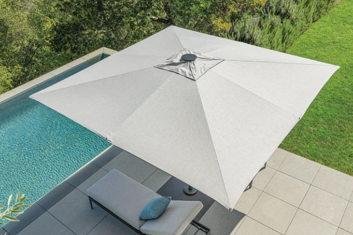 Top view of a large outdoor umbrella with a square light grey canopy that has a vent and flat finial next to a pool and grassy area