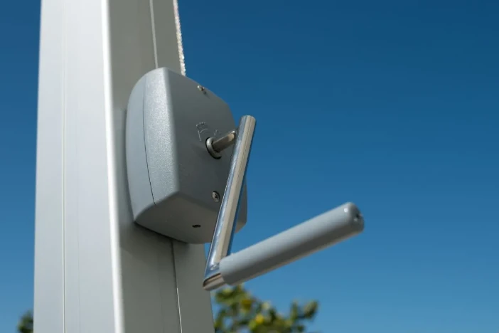 Close-up of crank lift for an aluminum framed cantilever umbrella on a clear day with blue skies