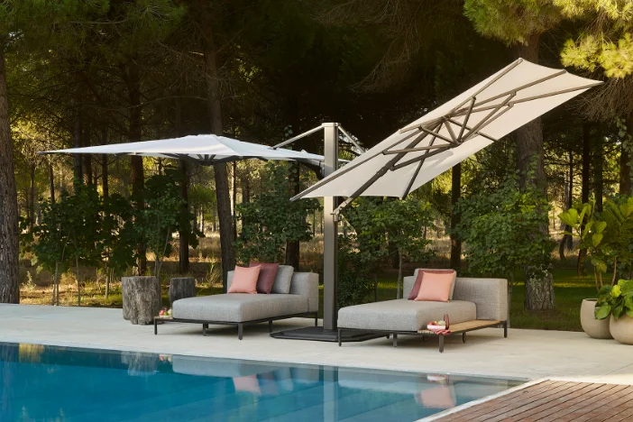 Multi-canopy cantilever umbrella with off-white fabric and bronze powder-coated frame and base shading two chaises poolside