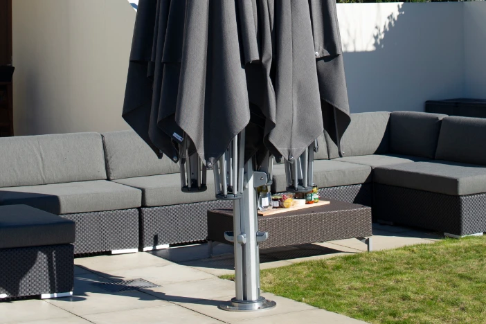 Close-up of closed multi-canopy aluminum patio umbrella with black fabric mounted on concrete