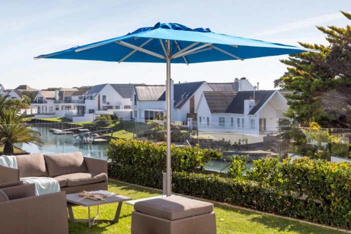 Aluminum market umbrella with a square bright blue canopy next to a patio lounge set near a canal