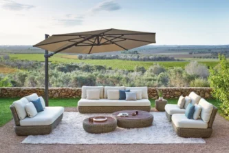 Cantilever outdoor umbrella with beige octagonal canopy providing shade for a lounge set on a terrace overlooking green fields