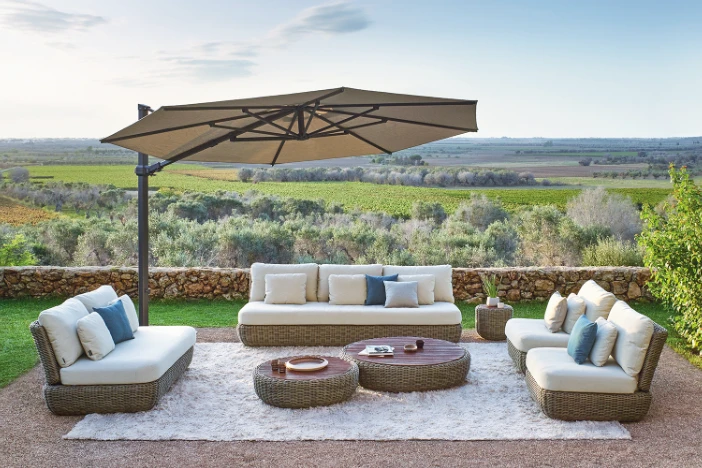 Cantilever outdoor umbrella with beige octagonal canopy providing shade for a lounge set on a terrace overlooking green fields