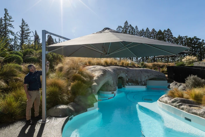 Man standing next to a cantilever umbrella adjusting the canopy next to a natural-shaped pool