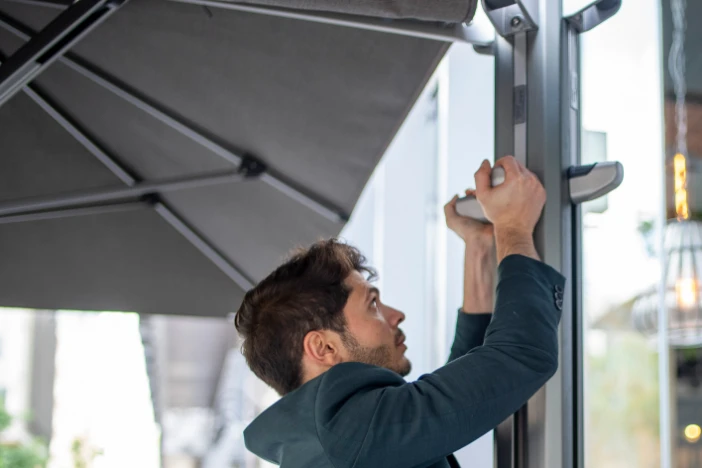 Young man in black hoodie raising the canopy of a large cantilever patio umbrella with an aluminum frame