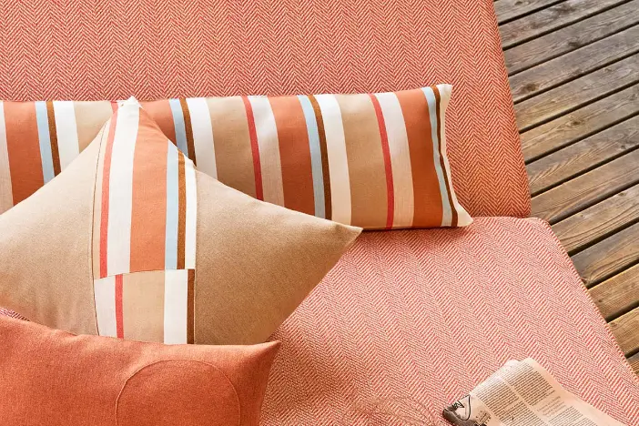 Peach colored array of solid and striped pillows on coordinated upholstered cushions on a wooden deck