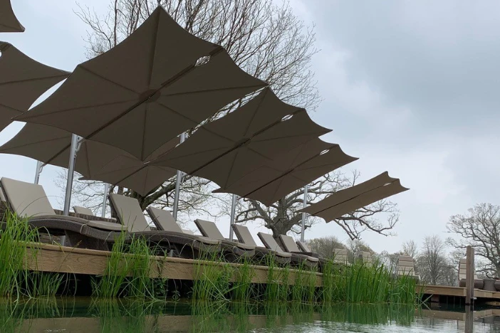 Line of cantilever umbrellas with square taupe canopies over loungers on a pier with a gloomy sky