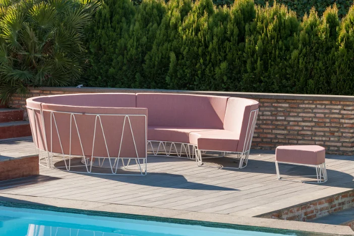 Circular patio sectional sofa and ottoman with white wireframe bodies and dusty pink upholstery on a poolside deck