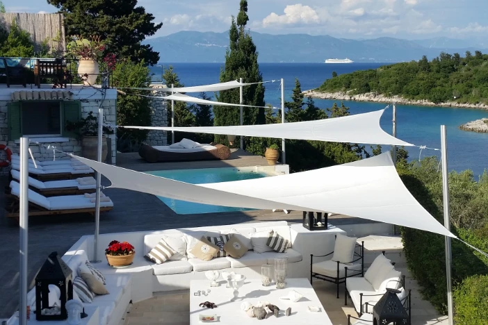 Four white triangular shade sails hung from poles over a deck near a body of water