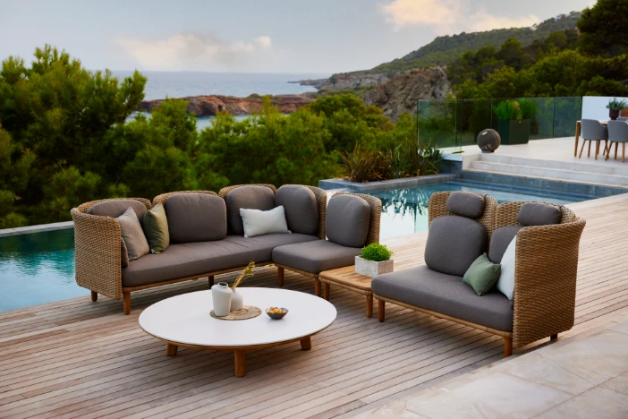 Brown outdoor wicker sectional sofa with round white topped coffee table on deck near a swimming pool