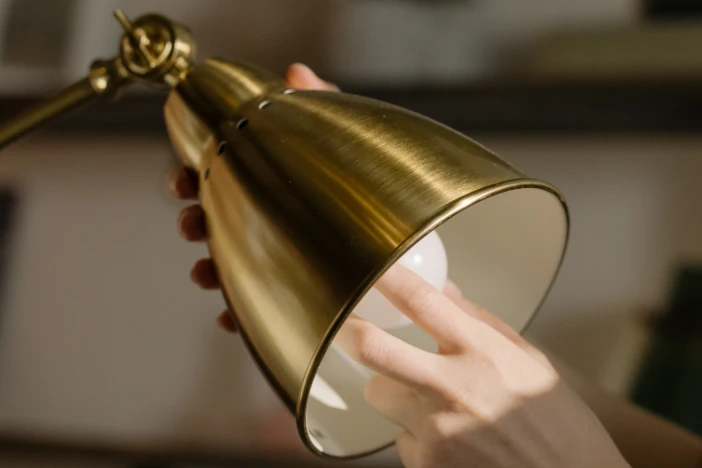 Close-up of a person changing the light bulb of a jointed brass lamp